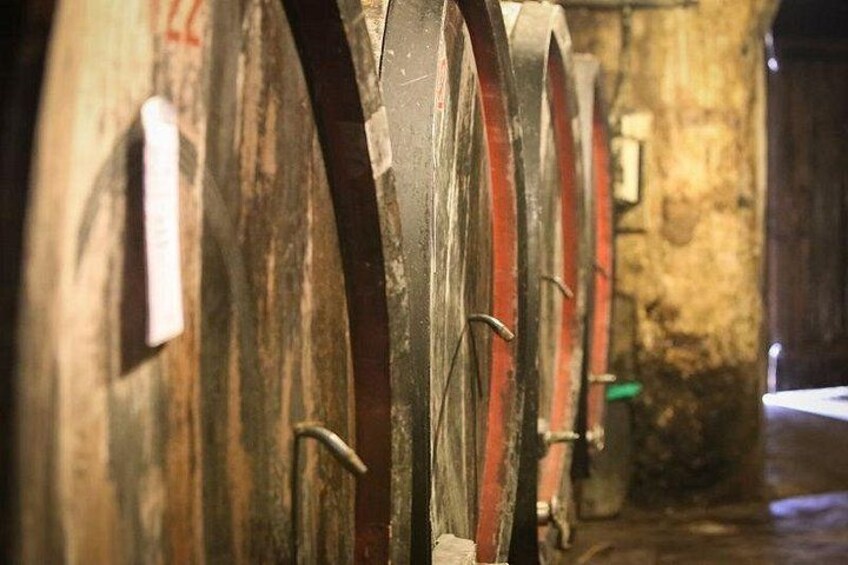 A row of old, weathered barrels with metal hooks, likely used for aging wine or similar liquids. 3