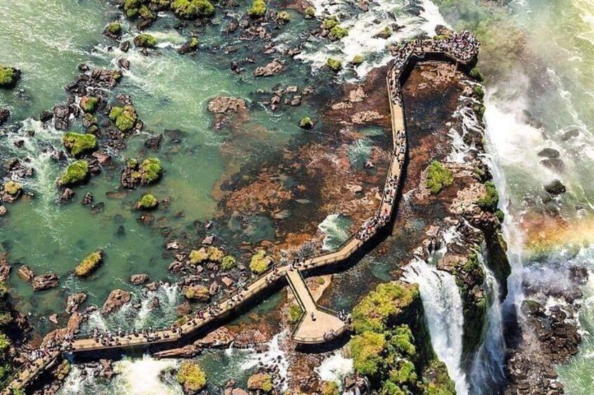 A coastal landscape with a wooden boardwalk, rocky outcrops, and a waterfall. 1