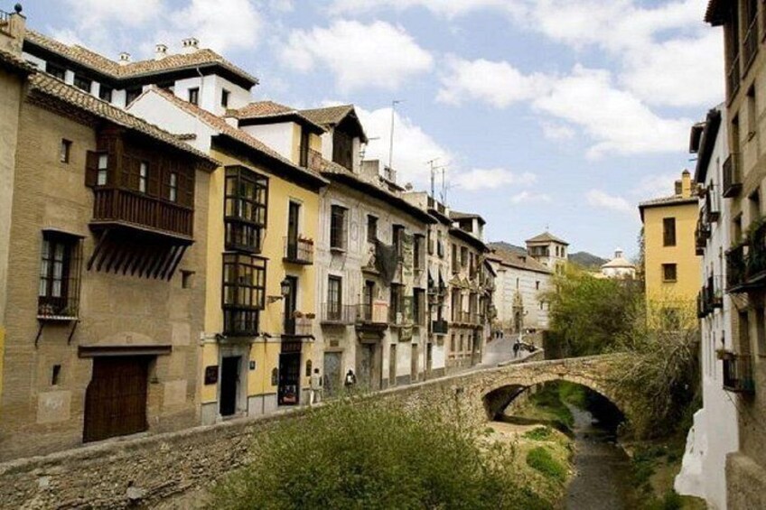 Una calle estrecha con edificios antiguos, un puente de piedra y un pequeño arroyo. 5