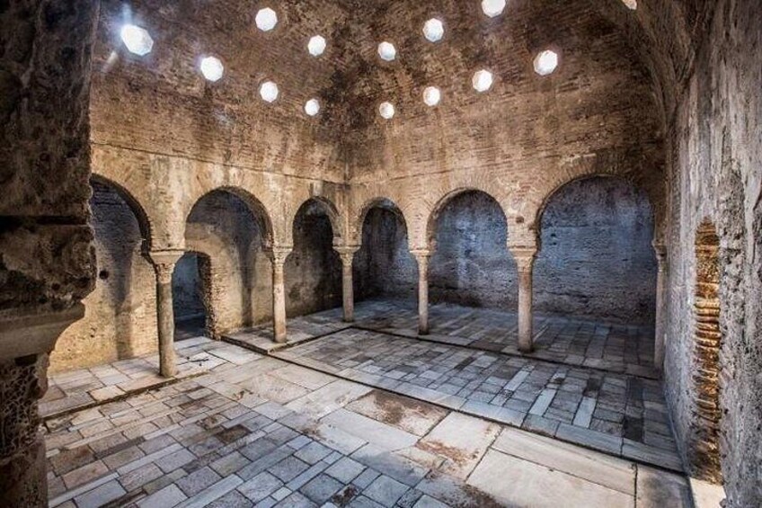 Un antiguo patio de piedra con arcos y columnas, iluminado por luces colgantes. 3