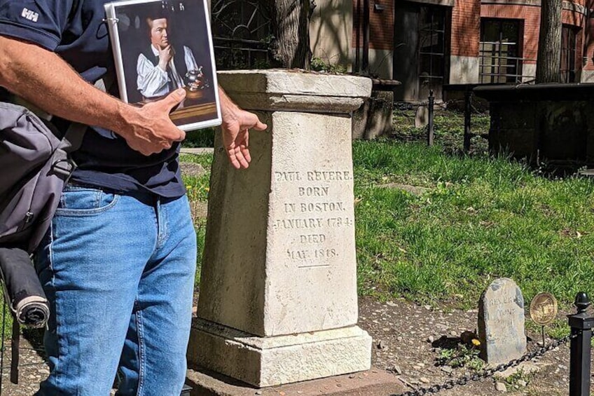 Un hombre sostiene un retrato enmarco junto a una lápida con la inscripción: "Paul Revere, nacido en Boston, fallecido en Roxbury, Massachusetts, 1794". 5