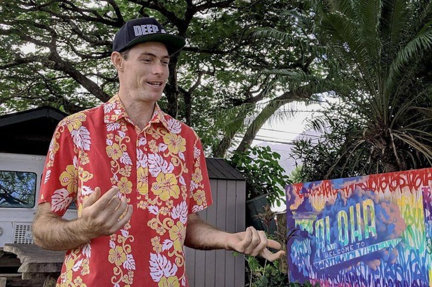 Une personne portant une chemise à fleurs rouge et une casquette, tenant une pancarte colorée avec du texte. 2
