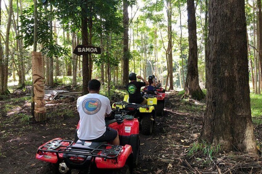 Une zone boisée avec un panneau indiquant « SAMOA » et des personnes conduisant des quads. 2