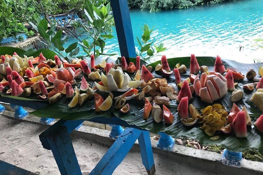 Variedad de frutas expuestas sobre una mesa al aire libre cerca del agua. 1