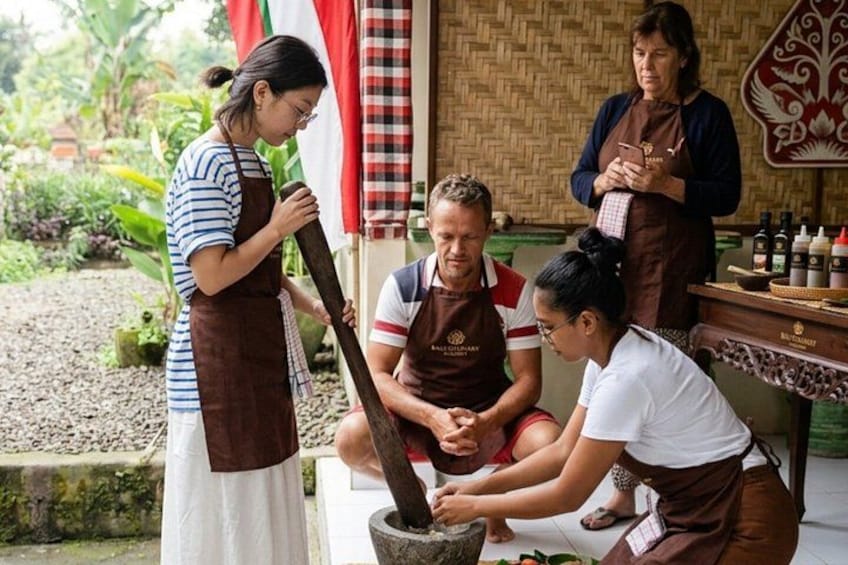 People in aprons grinding spices outdoors. 1