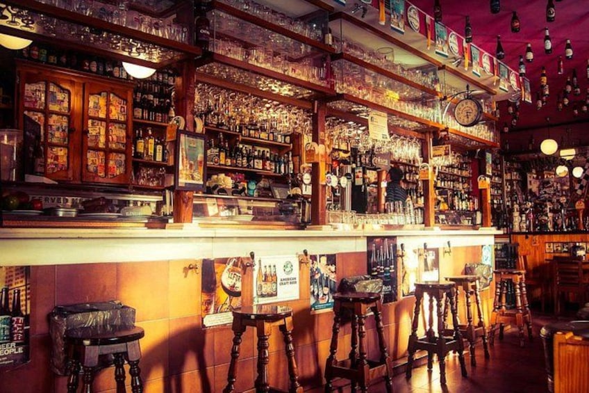 Un bar con scaffali di legno pieni di bottiglie e bicchieri, una sveglia e degli sgabelli. 5