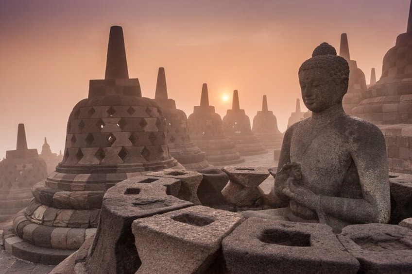 En sten Buddhastatue i en historisk lokalitet med gamle bygninger og solnedgang i baggrunden. 2