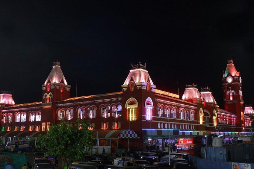 A brightly lit historic building with multiple domes and towers, surrounded by parked cars and a tree. 1
