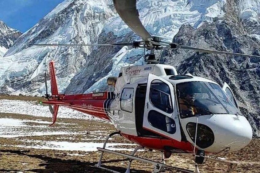 A helicopter with a red and white color scheme parked on a snow-covered ground with mountains in the background. 3