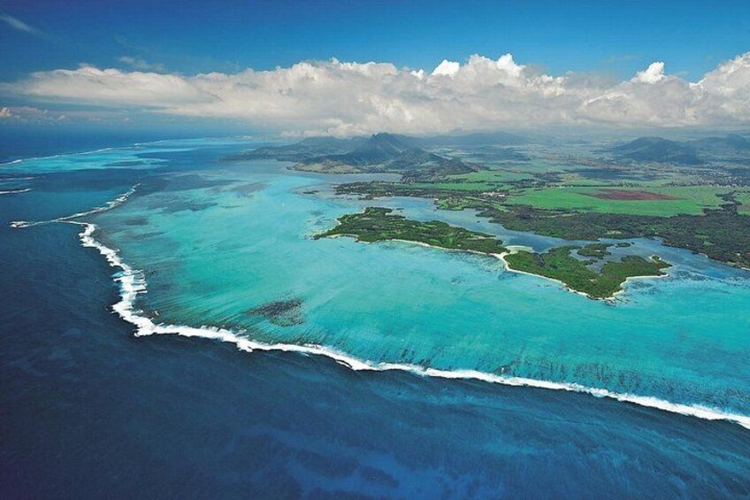 An aerial view of a coastal landscape with clear turquoise waters, a white sandy beach, and green vegetation. 5