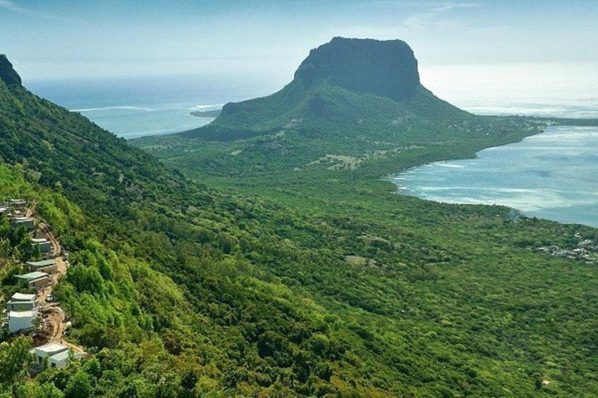 A mountainous landscape with a prominent peak, lush greenery, and a coastal area with buildings along the shore. 1