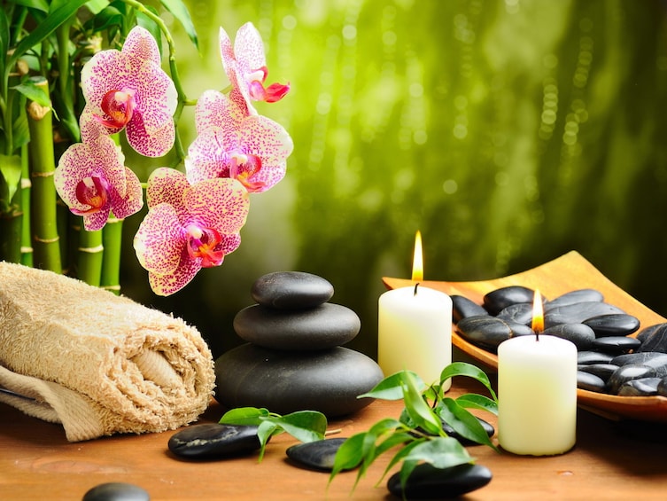A spa setting with a rolled towel, black stones, candles, and pink orchids. 2