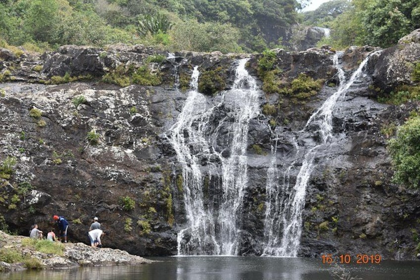 A waterfall cascading over a rocky cliff into a calm pool, surrounded by lush greenery. 1