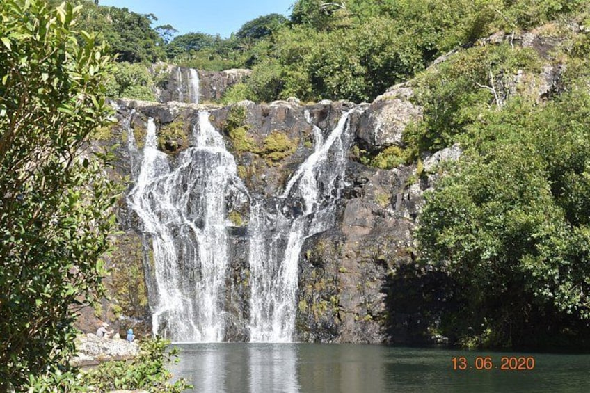 A waterfall cascading over rocks into a calm body of water, surrounded by lush greenery. 2