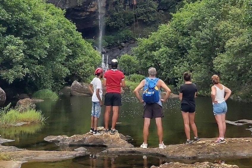 Een groep mensen staat op rotsen naast een waterval in een bebost gebied. 2