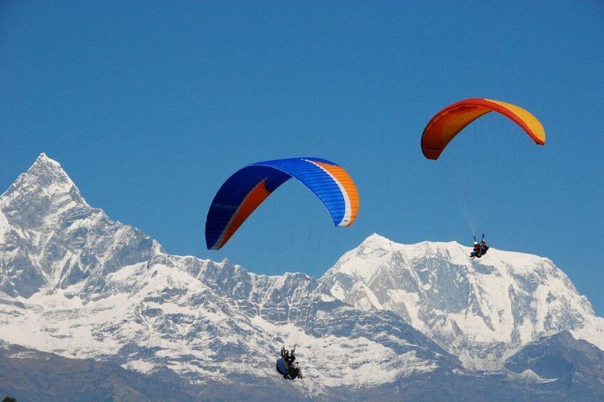 Three paragliders with colorful canopies flying over snow-capped mountains. 1