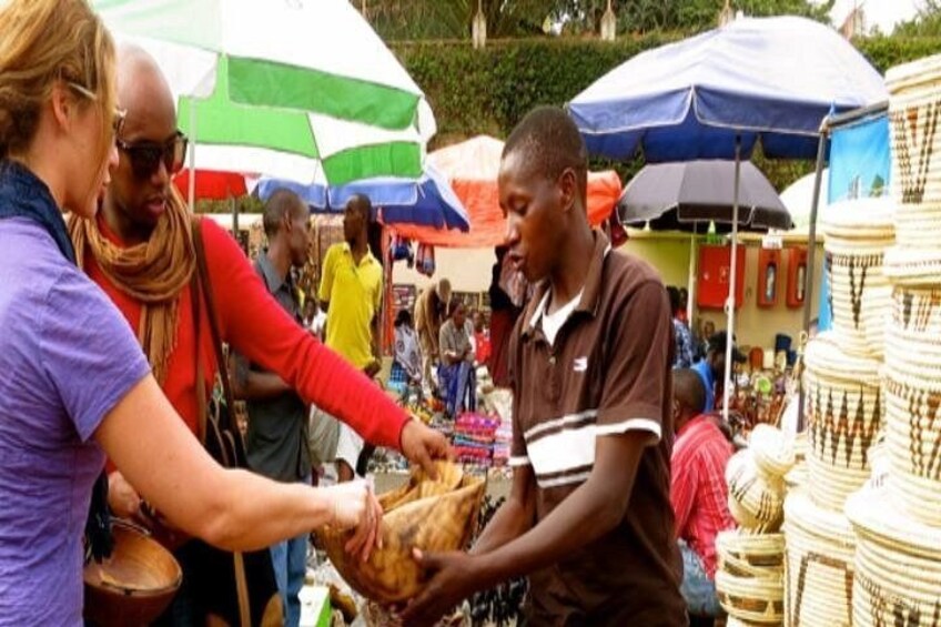 A market scene with people interacting, a man holding a large drum, and various items for sale under colorful umbrellas. 2