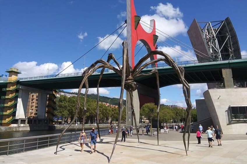 Une promenade piétonne agrémentée d’une grande sculpture métallique, d’un pont et d’un bâtiment moderne. 3