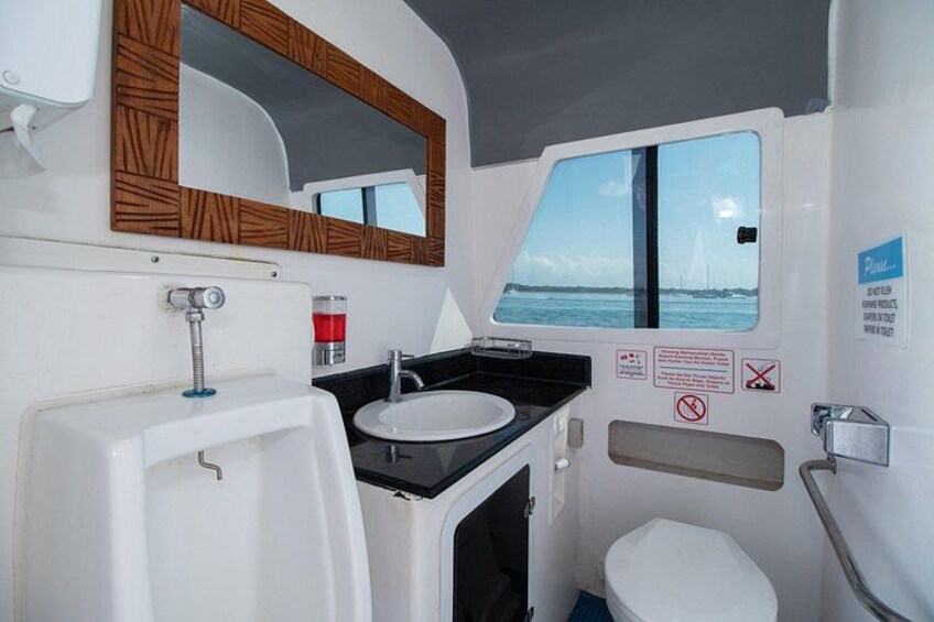 A compact bathroom with a white sink, a mirror with a wooden frame, a toilet, and a window with a view of the sea. 5