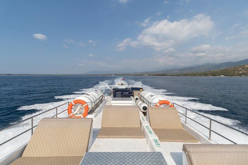 A boat deck with cushioned seating, life rings, and a clear view of the water and distant land. 2