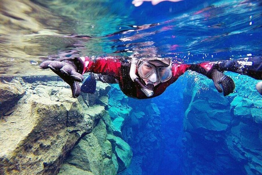A person scuba diving underwater with rocks and clear blue water. 1