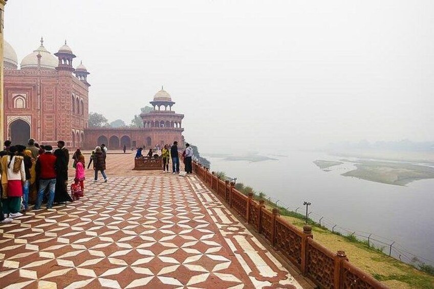 A Mughal architecture with a patterned walkway, a large body of water, and a distant view of the Taj Mahal. 3