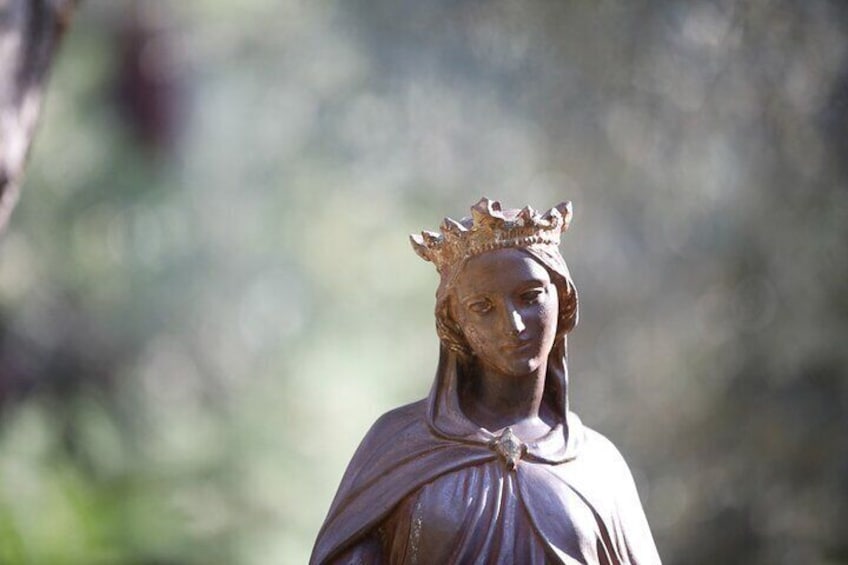Une statue représentant une figure couronnée, se détachant sur un arrière-plan naturel flou. 1