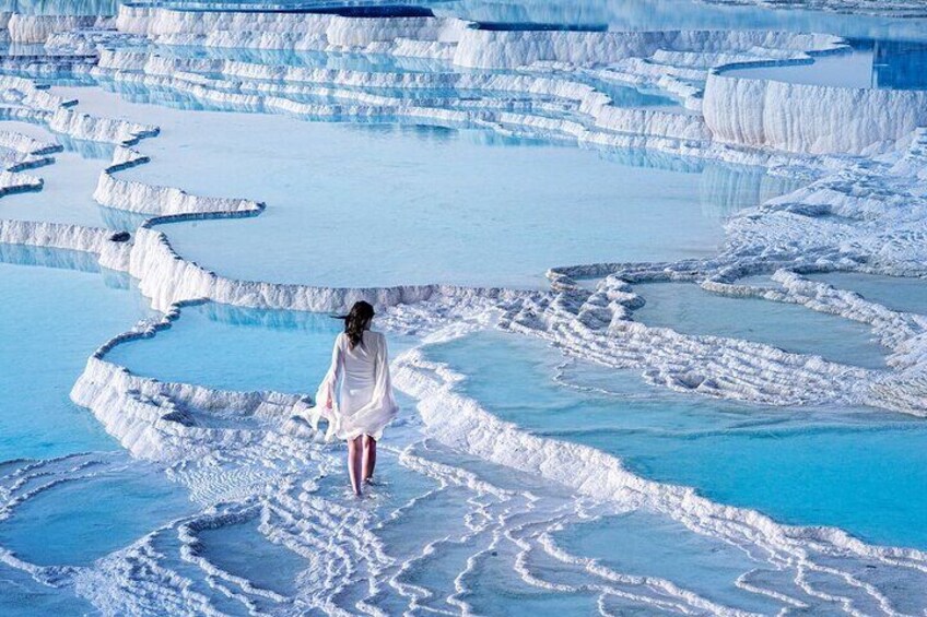 A person in a white dress walking on terraced mineral formations. 1