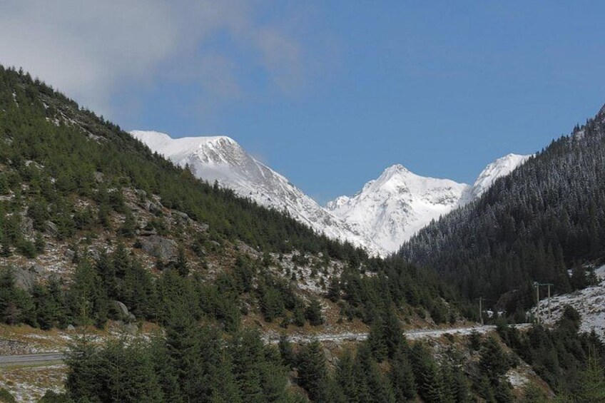 A mountainous landscape with snow-covered peaks, dense forests, and a clear sky. 2