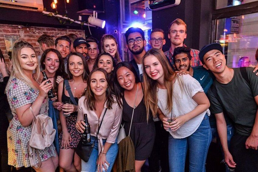 Een groep mensen in een donkere ruimte, mogelijk een bar of club, met bakstenen muren en een raam op de achtergrond. 4