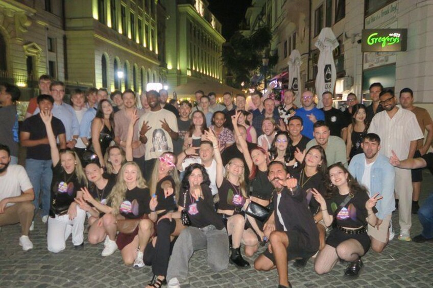 A group of people posing for a photo on a cobblestone street at night. 1