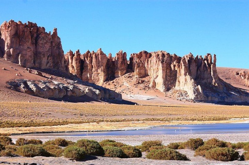 Wüstenlandschaft mit Felsformationen, einem kleinen Gewässer und vereinzelter Vegetation. 2
