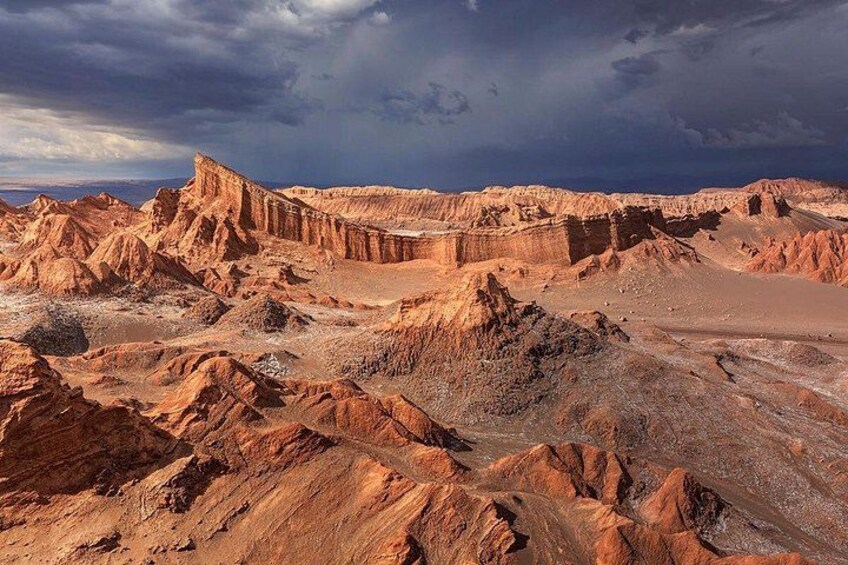 A rugged desert landscape with eroded rock formations and a dramatic sky. 3