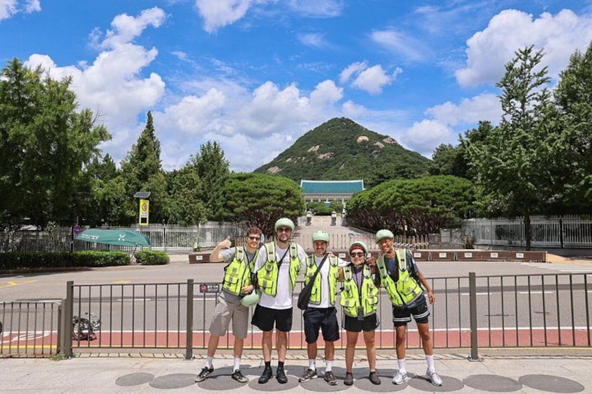 A group of people in safety vests standing in a fenced area with a mountain in the background. 4