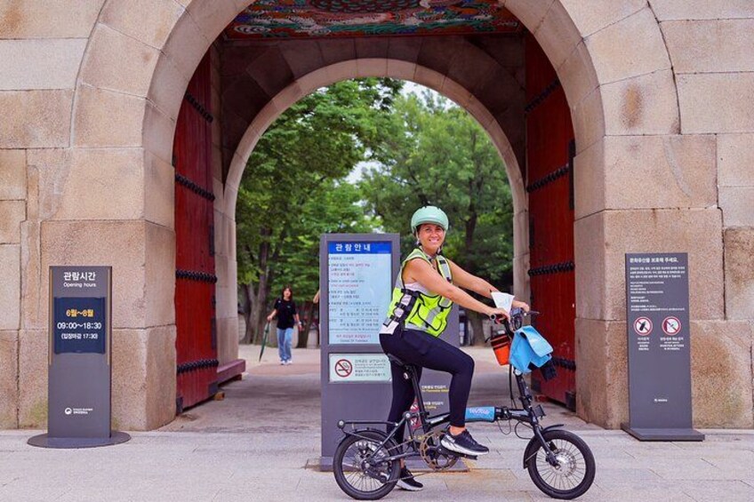 A person riding a bicycle under a stone archway with informational signs. 3