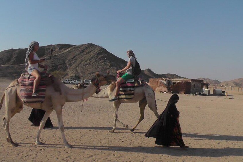 Dos camellos con jinetes en un paisaje desértico con colinas al fondo. 3