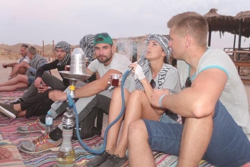 Un grupo de personas sentadas sobre una manta al aire libre, con un narguile en primer plano. 4
