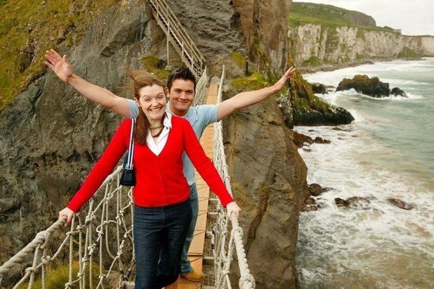 A person standing on a rope bridge over a cliff with a body of water below. 2