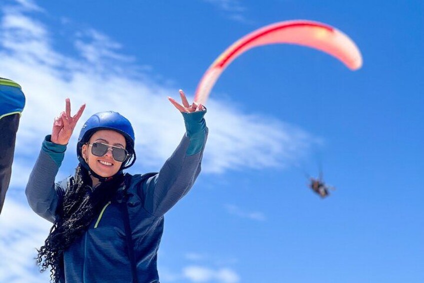 Een persoon paraglidet met een rode kap, draagt een helm en een jas, voor een helderblauwe lucht. 5