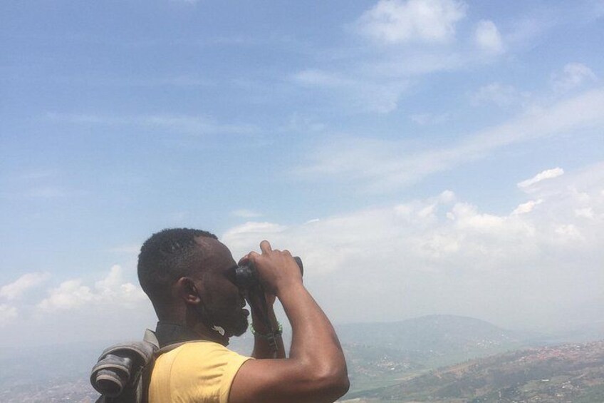 Iemand houdt verrekijkers vast en kijkt uit over een landschap met verre bergen en een heldere lucht. 4