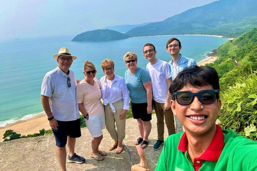 Un grupo de personas de pie en un acantilado con vistas a un paisaje costero y montañas distantes. 3