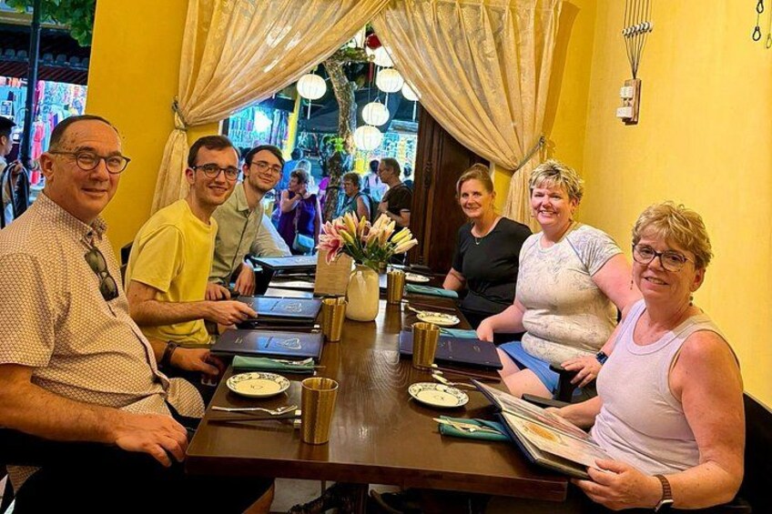 Un grupo de personas sentadas alrededor de una mesa con platos, tazas y un florero. 4