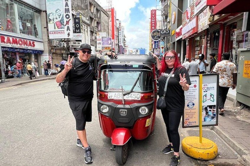 En röd, automatisk rickshaw på en stadsgata, omgiven av människor. 5