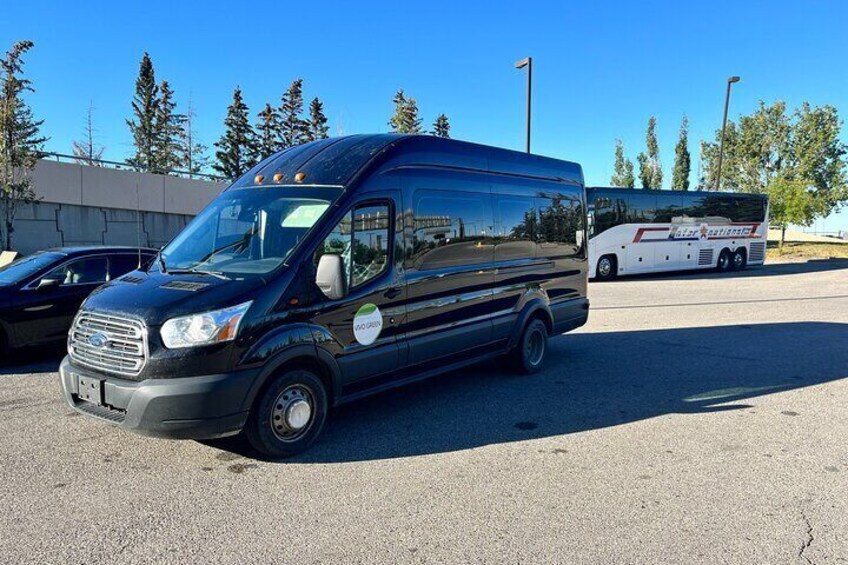 A black van parked in a lot with a white bus in the background. 3