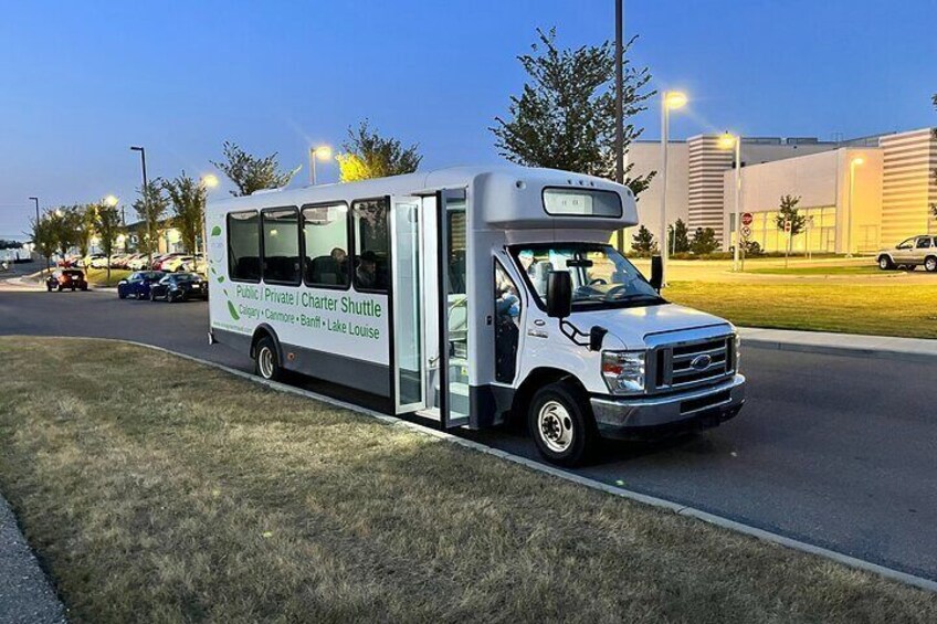 A charter shuttle with 'Public/Private Charter Shuttle' written on the side, parked on a street with buildings in the background. 2