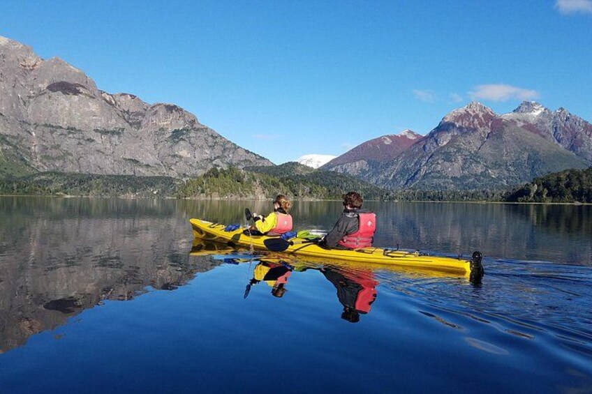 Two people kayaking on a calm lake with mountains in the background. 1