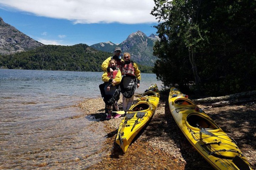 A group of people near kayaks by a lake with mountains in the background. 4