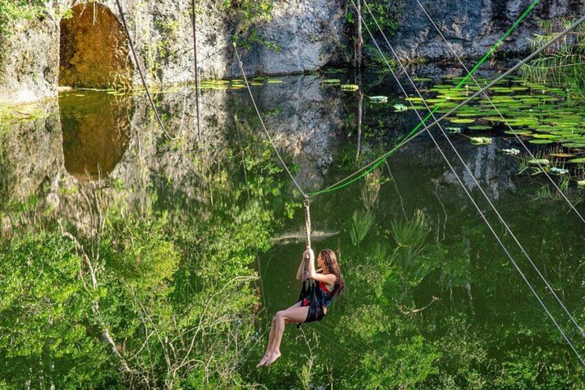A person swinging on a rope over a body of water with lily pads and greenery around. 2
