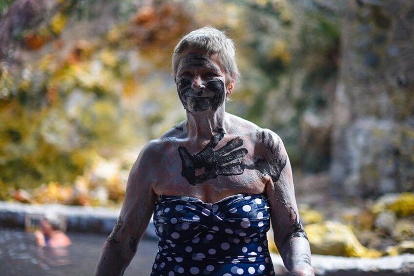 A person with black paint on their face and arms, wearing a polka dot dress, standing by a body of water with autumn foliage in the background. 4