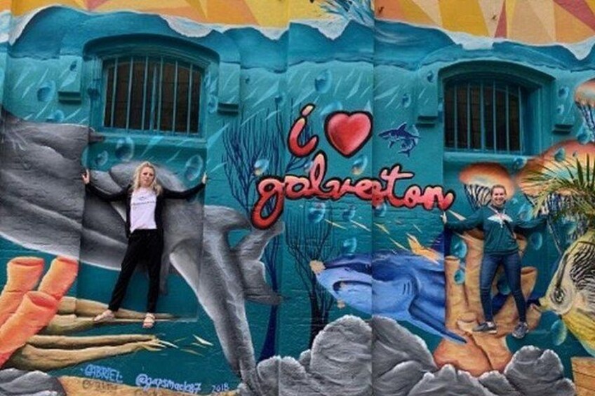 Un mural con un tiburón, una persona de pie sobre una roca y el texto 'I love galveston'. 2